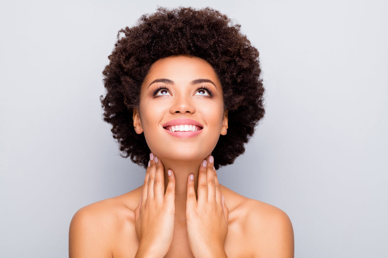 Woman with curly hair smiling and looking upward, hands on her neck, representing hormonal balance and healthy estrogen metabolism