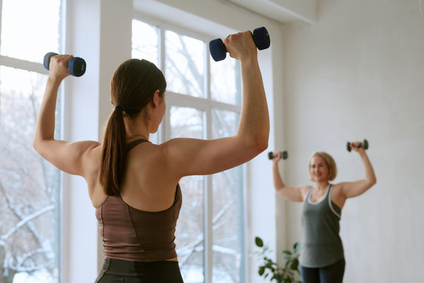 Two women strength training with dumbbells in a bright room, a key part of a healthy GLP-1 therapy protocol.