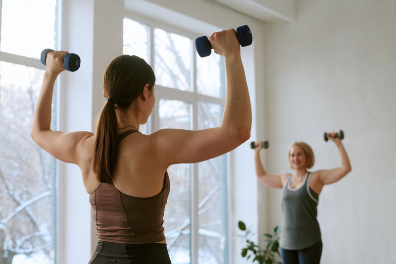 Two women strength training with dumbbells in a bright room, a key part of a healthy GLP-1 therapy protocol.