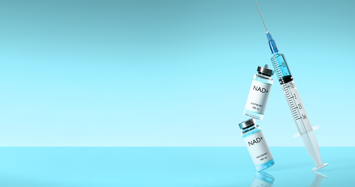 Two NAD+ 1000mg injection vials alongside a medical syringe on a reflective light blue surface.
