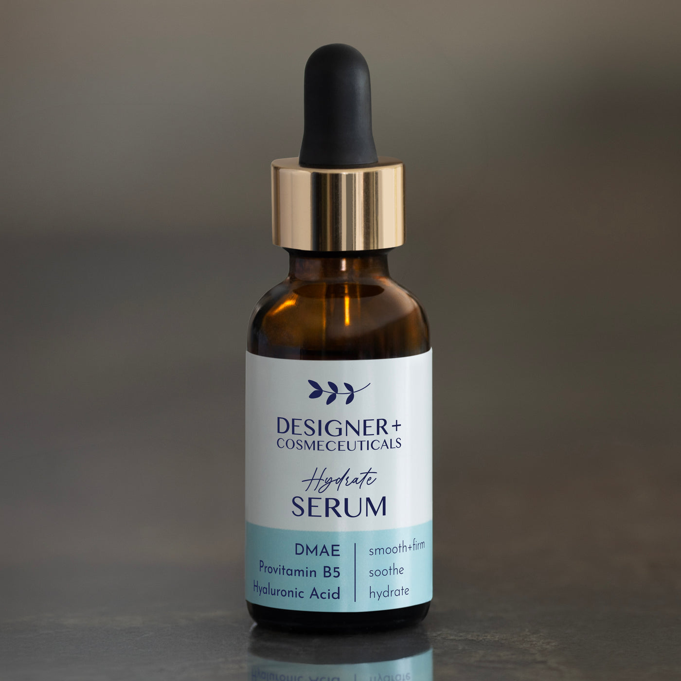 Designer+ Cosmeceuticals Hydrate Serum with DMAE, Provitamin B5, and hyaluronic acid in a brown glass dropper bottle, on a reflective surface with a dark background