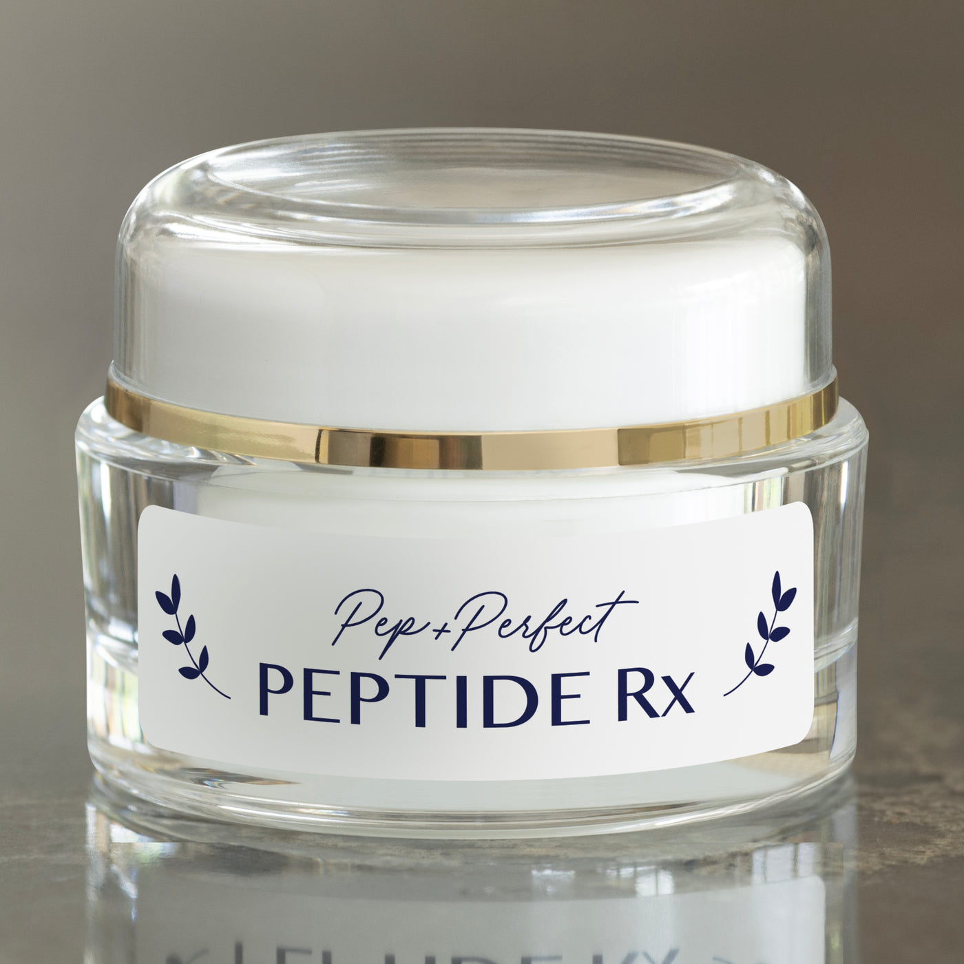 Pep+Perfect Peptide Rx face cream in a clear glass jar with a white lid and gold band, on a reflective surface with a neutral background