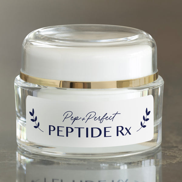 Pep+Perfect Peptide Rx face cream in a clear glass jar with a white lid and gold band, on a reflective surface with a neutral background