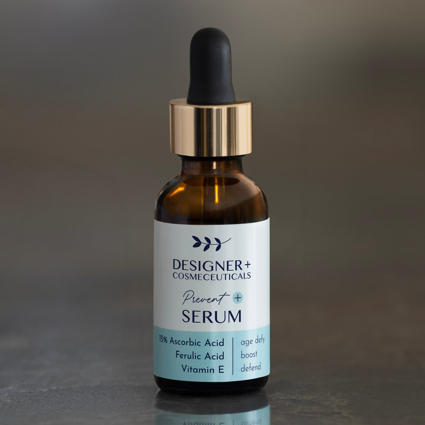 Designer+ Cosmeceuticals Prevent Serum with 15% ascorbic acid, ferulic acid, and vitamin E in a brown glass dropper bottle, on a reflective surface with a gray background