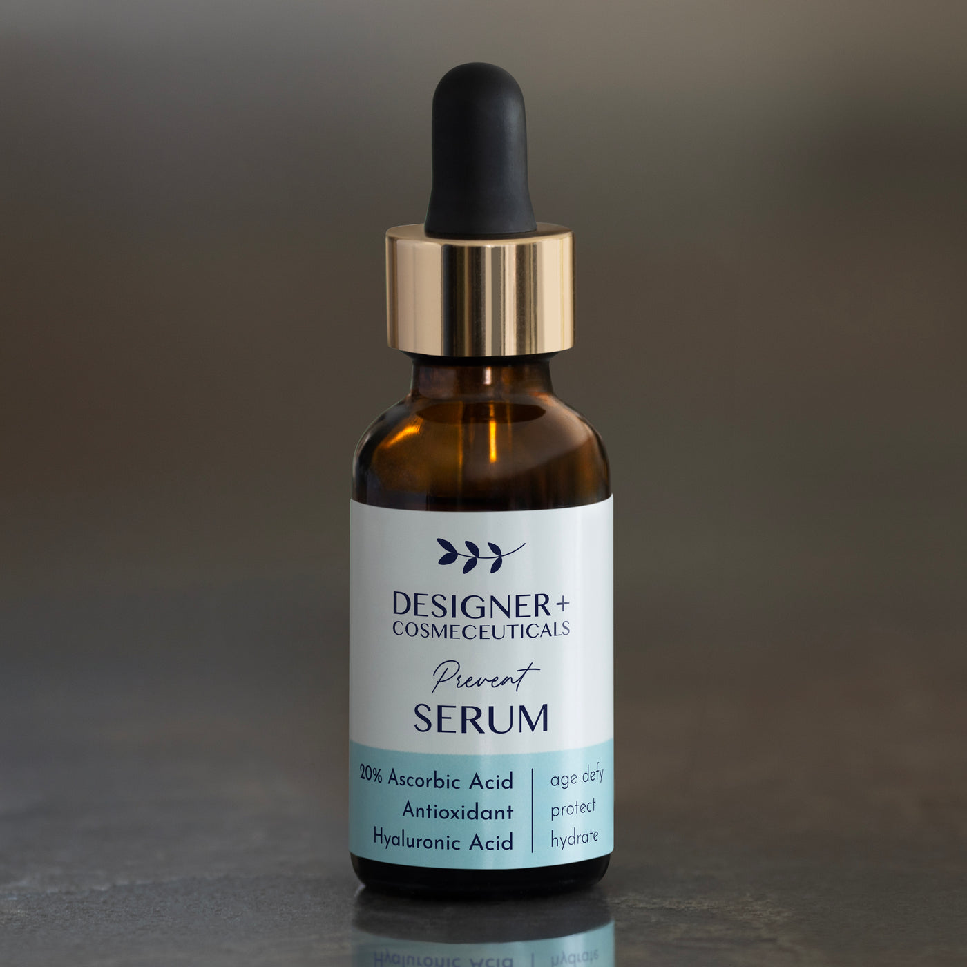 Designer+ Cosmeceuticals Prevent Serum with 20% ascorbic acid, antioxidants, and hyaluronic acid in a brown glass dropper bottle, on a reflective surface with a gray background